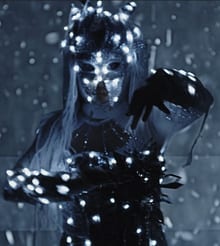 Un esprit masqué au costume constellé de petites lumières blanches, dans une lumière bleutée