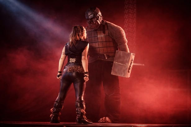 Une guerrière de dos fait face à un ogre géant armé d'une massue, dans une lumière rouge
