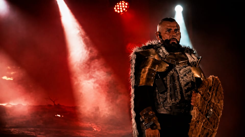 Le Roi en armure dorée et cape de fourrure, sous des faisceaux de lumière rouge et blanche